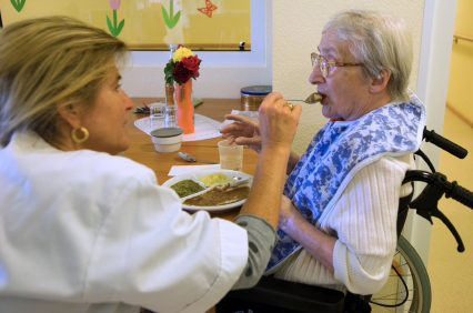 Nurse feeding a patient that is sitting in a wheelchair.