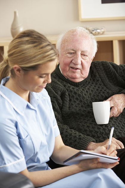 Caregiver writing notes down while sitting next to a patient that is drinking coffee.