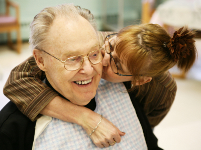 Wife hugging and giving elderly patient a kiss.